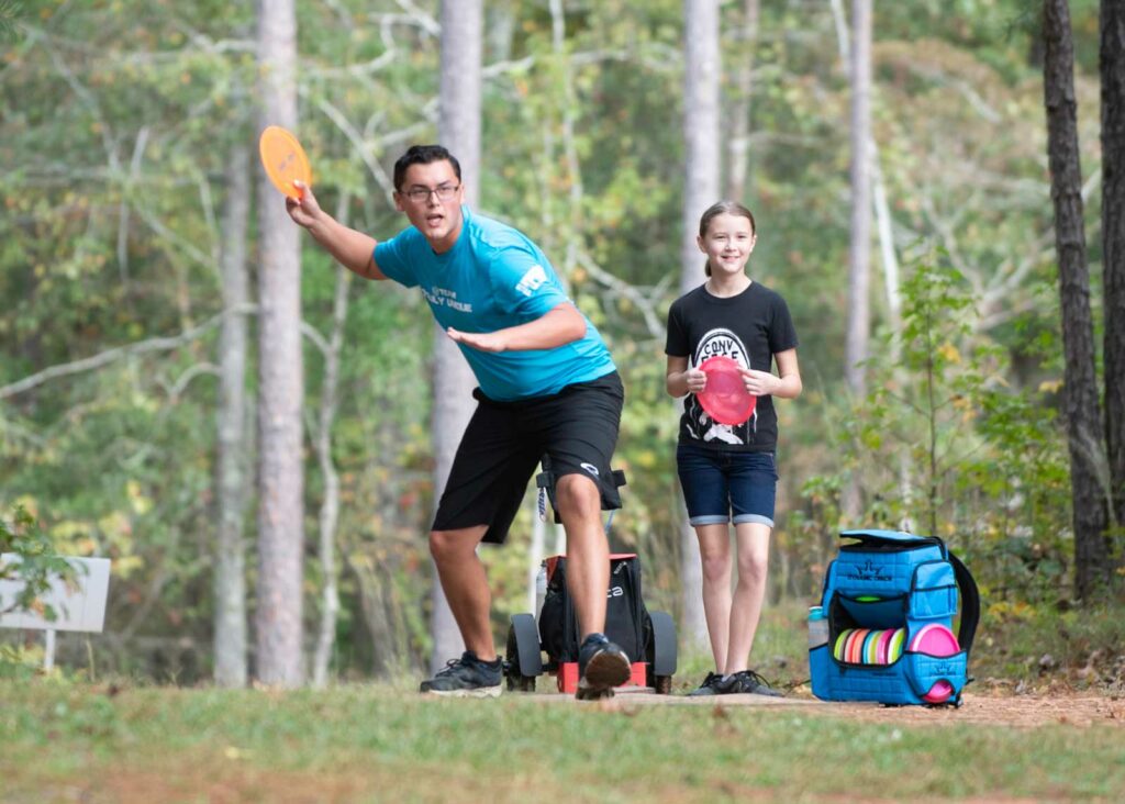 Adult man and young girl playing disc golf together, in position to throw the frisby.